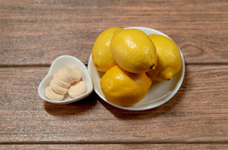 four lemons with orange vitamin c tablets in different dishes on a wood table top viewの写真素材