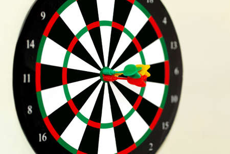 Perfect shots of darts at the target darts of different colors red yellow and green with cream backgroundの写真素材