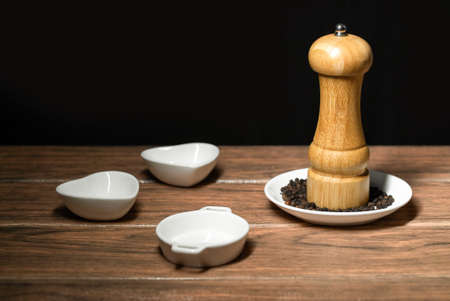Black pepper mill with whole peppercorns on a white ceramic plate and black backgroundの写真素材