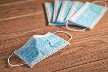 Disposable surgical masks with ear-loop and many mask in background on a wood close-upの写真素材