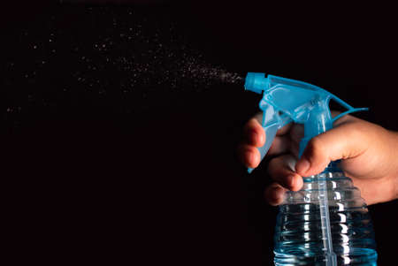 A girl hand spraying a blue spray with cleaning product with black backgroundの写真素材