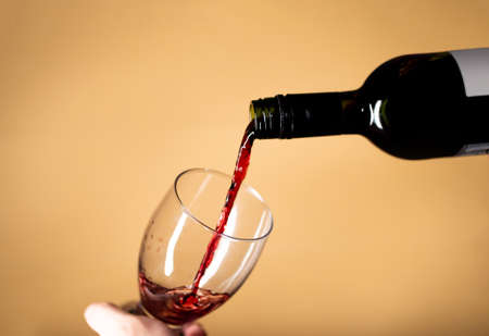 Serving a glass of red wine splashing onto the glass beige background colorの写真素材
