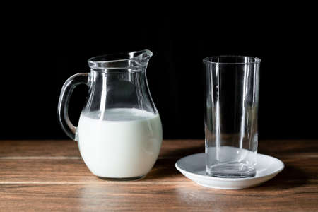 An empty glass cup and a jar of cow's milk on a wooden tableの写真素材