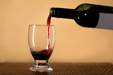 Serving a glass of red wine splashing onto the glass in a table beige backgroundの写真素材