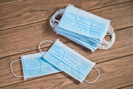 Blue disposable surgical masks with ear-loop and many masks on a table wood close-upの写真素材