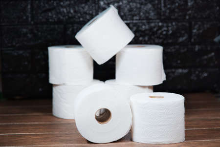 Many rolls of white disposable bathroom toilet paper on a brown wooden tableの写真素材