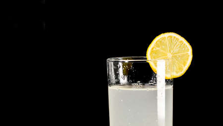 A glass of cold lemonade with a piece of yellow lemon with black color background close-upの写真素材