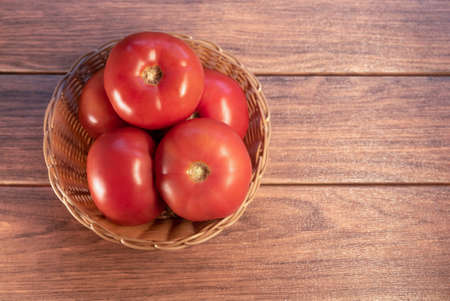 many fresh red tomato in a woven basket close-up wood backgroundの写真素材