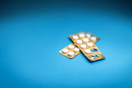 one open white pill pack and one sealed packet with a blue colored background close-up