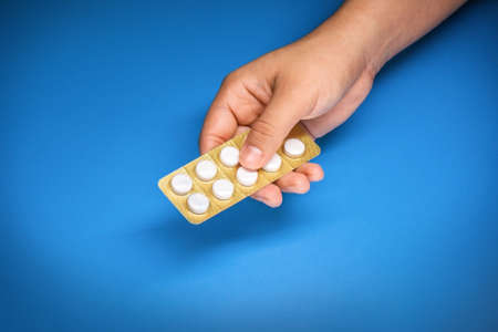 a girl's hand giving a pack of white pills with a blue backgroundの写真素材