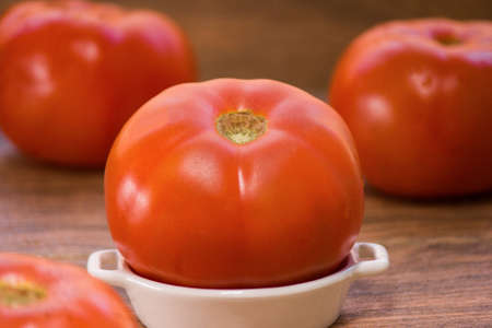 a fresh large red tomato on a white ceramic plate and more tomatoes in the backgroundの写真素材