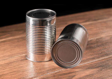 Two long silver colored canned goods on wooden table with black background close-upの写真素材