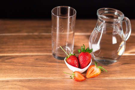 fresh red strawberries cut in half with a glass cup and glass jar with water on brown wooden surfaceの写真素材