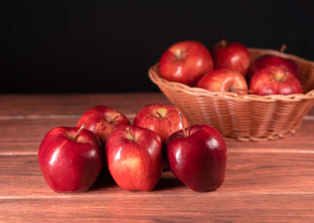 Many fresh red apples with brown basket with more apples in the background close-upの写真素材