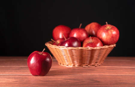 Single red apple with brown basket full of apples in the background