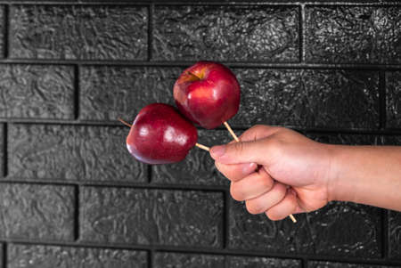 Man's hand holding red apples with wooden sticks on a black backgroundの写真素材