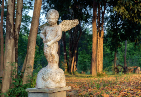 Old and dirty statue of cupid standing in the garden.の写真素材