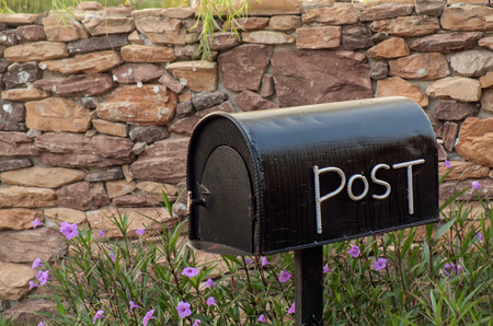 Plain black mailbox in bushes with stone wall background.の写真素材