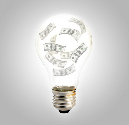 Light bulb with hundred dollars inside on gray background. Business concept.の写真素材