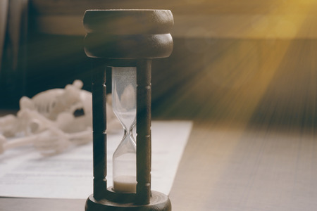 Close up of vintage hourglass on the table. Dim light. Vintage style.
