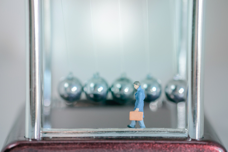 View of miniature toy, businessman walking with momentum pendulum background. Soft blue filter.の写真素材