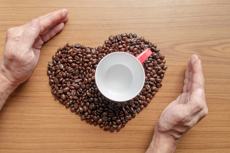 Red coffee cup with coffee bean and hand on wood background.の写真素材