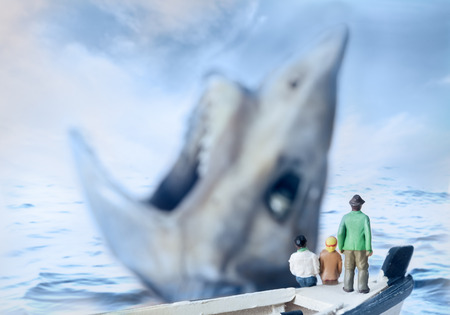 View of miniature toy, young man and girl sit on boat looking shark.の写真素材