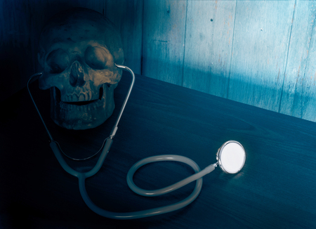 View of stethoscope and skull on wood background. Dark blue tone.の写真素材