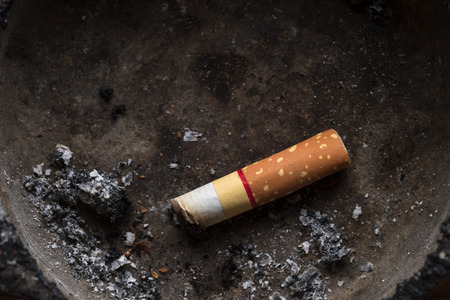 Close up of cigarette in dirty ashtray. Dark tone.