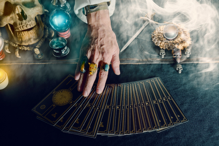 Hand of fortune teller and tarot card on the table under candlelight. Dark tone.