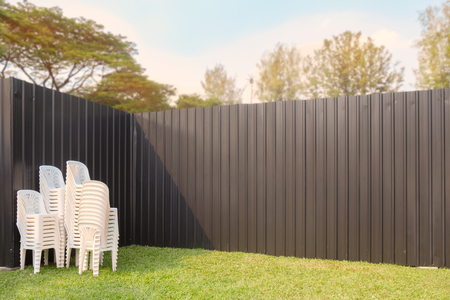 Heap of plastic chairs on grass with iron wall.の写真素材