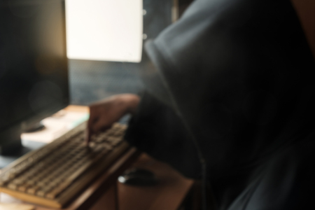 Blur of hooded man using computer.