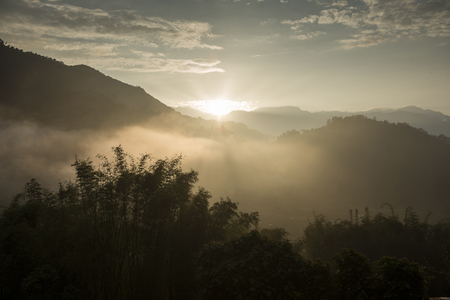 Morning sun rays through the fog over mountain slopes.の写真素材