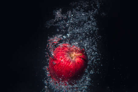 Apple falling in water isolated on black background.の写真素材