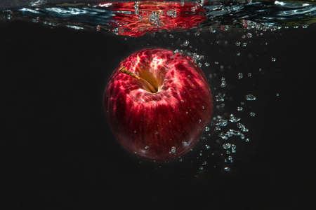 Apple falling in water isolated on black background.の写真素材