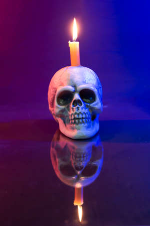 Close-up of colorful human plastic skull  with burning candle on head. Halloween image.
