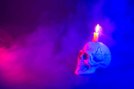 Close-up of colorful human plastic skull  with burning candle on head. Halloween imageの写真素材