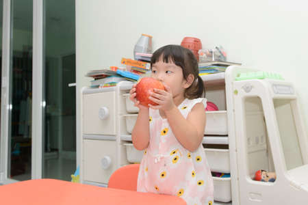 Little Asian girl  eating red apple at homeの写真素材