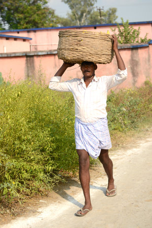 NALANDA,BIHAR, INDIA-28 October 2021: Man carrying basket on his head and walking on the road.のeditorial素材