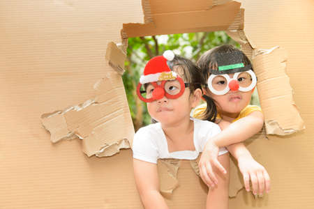 Cute little boy and girl wearing funny Christmas glasses making funny faces in torn paper wall.の写真素材
