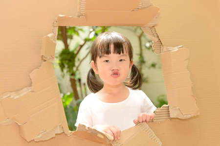 Cute little girl making funny faces in torn paper wall.の写真素材