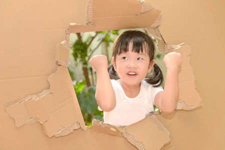 cute little child girl raising a fist
in the torn paper wall.の写真素材