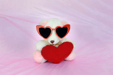 teddy bear wearing heart-shaped sunglasses with red heart on pink backgroundの写真素材