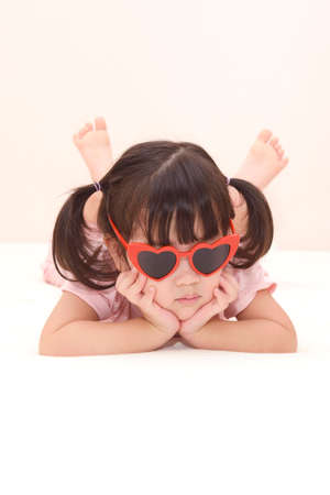 A young Asian girl wearing heart-shaped sunglasses lies on the floor with her hands on her chin.  valentine's day conceptの写真素材