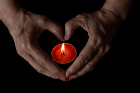 shapes heart with hands over burning candle on dark backgroundの写真素材