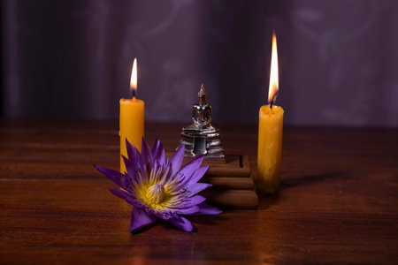 Close-up of a little Buddha statue ,water lily and burning candles on the table.