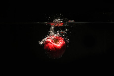 Sweet red apples fall into the water with a splash and air bubbles on the black background.の写真素材