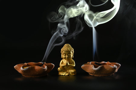 Close-up of a little Buddha statue with the smoke of an extinguished candle  on the back backgroundの写真素材