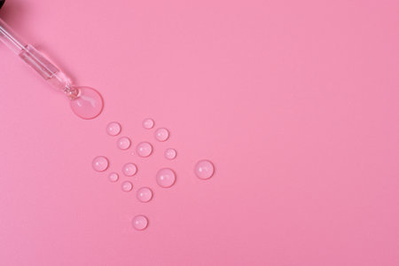 Drops of transparent liquid are squeezed out of a pipette on a pink backgroundの写真素材