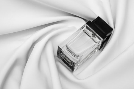 A transparent bottle of perfume with a black square cap, on a white cloth.の写真素材